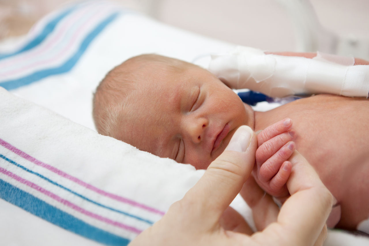Baby sleeping with mother holding his hand.